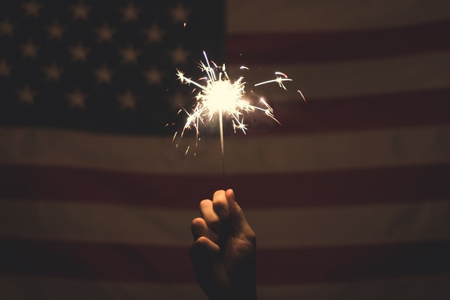 Person holding sparkler in front of USA flag Person holding sparkler in front of USA flag
